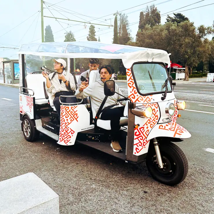 A MAZE guide with a headset driving three guests through Lisbon in a white electric tuk-tuk with the orange MAZE pattern