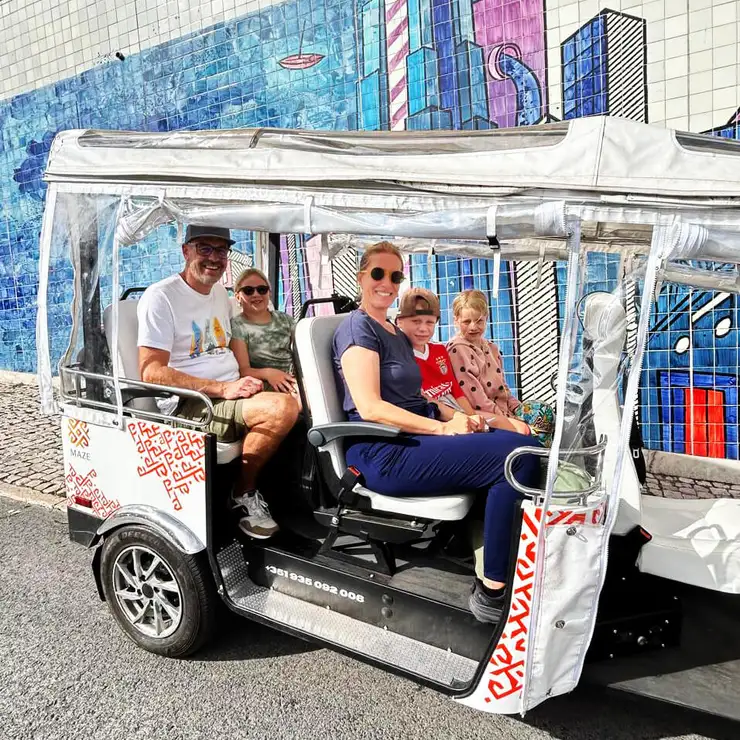 A family of five aboard a MAZE tuk-tuk in front of a blue tile mural in Lisbon